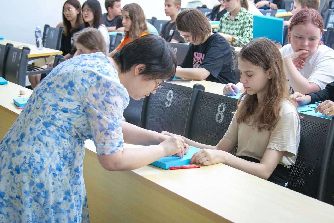 Ученики ZHIDAO за партами на занятии, преподаватель помогает разобрать задание
